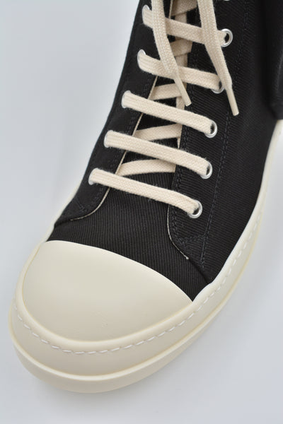 Cargo sneakers featuring a black cotton denim upper, above ankle height, eight eyelets, shoe lace, zipped cargo side pockets, milk white leather toe caps and shark tooth rubber soles